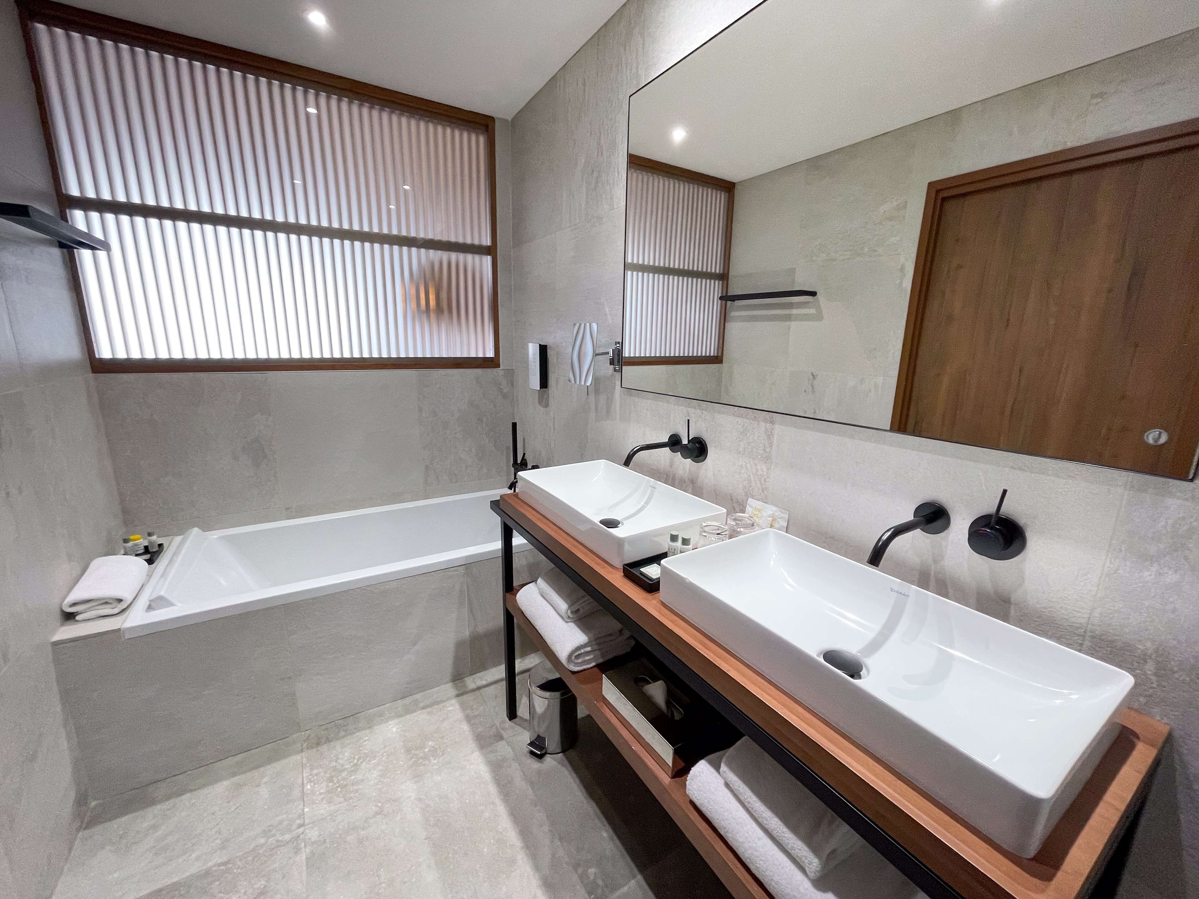 A modern bathroom with two sinks, a bathtub, and a large mirror.