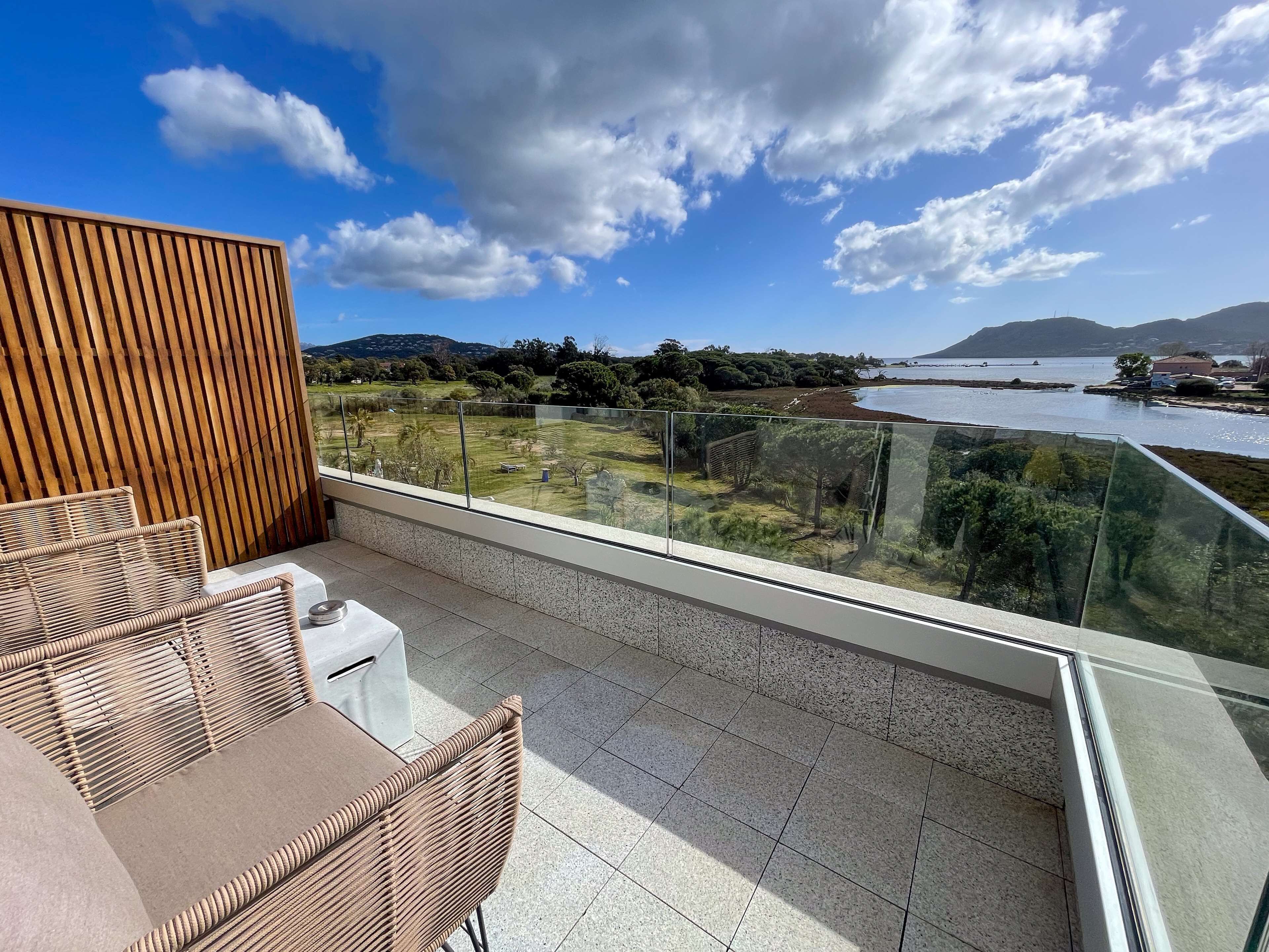 Een balkon met uitzicht op een meer, een houten wand en een zithoek met een tafel en stoelen.
