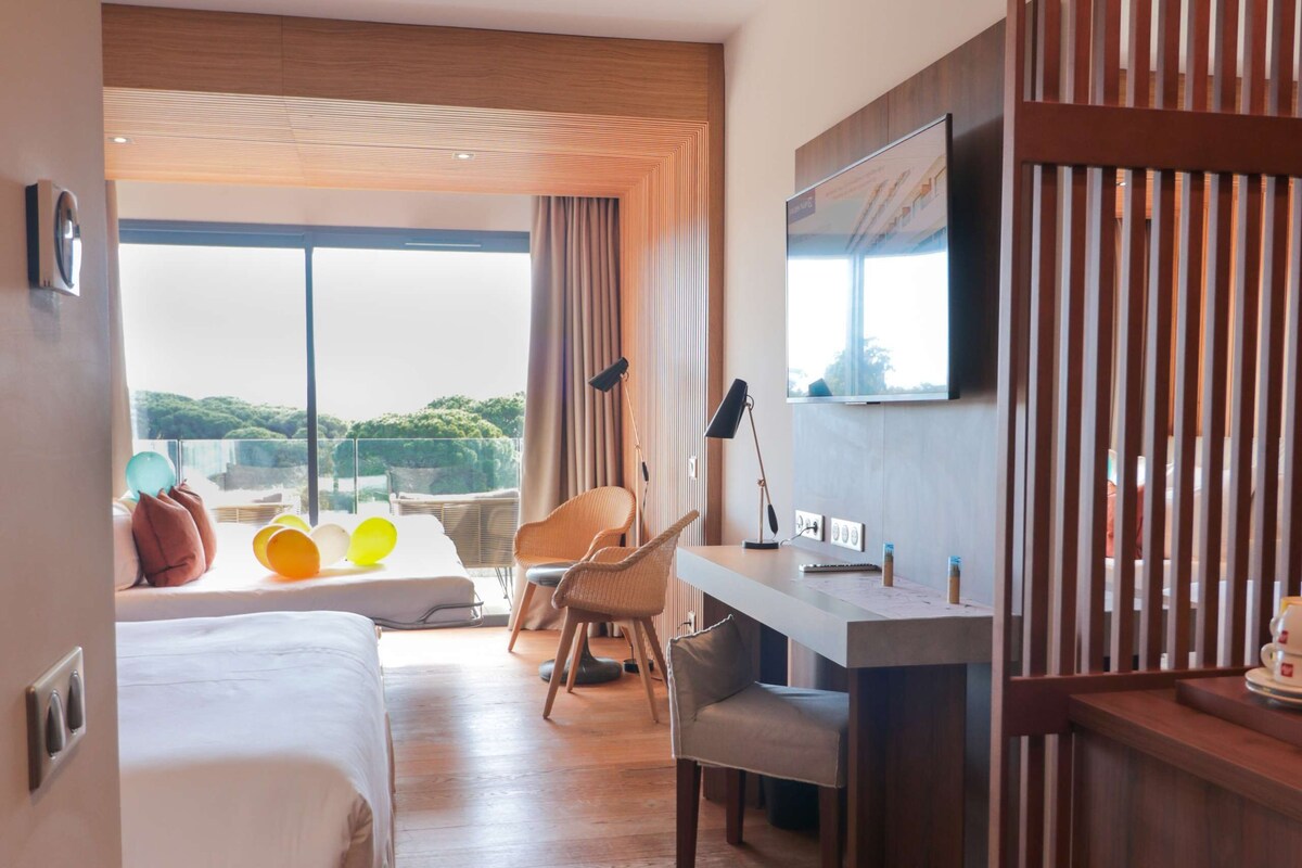A hotel room with a bed, desk, chair, and a large window with a view.