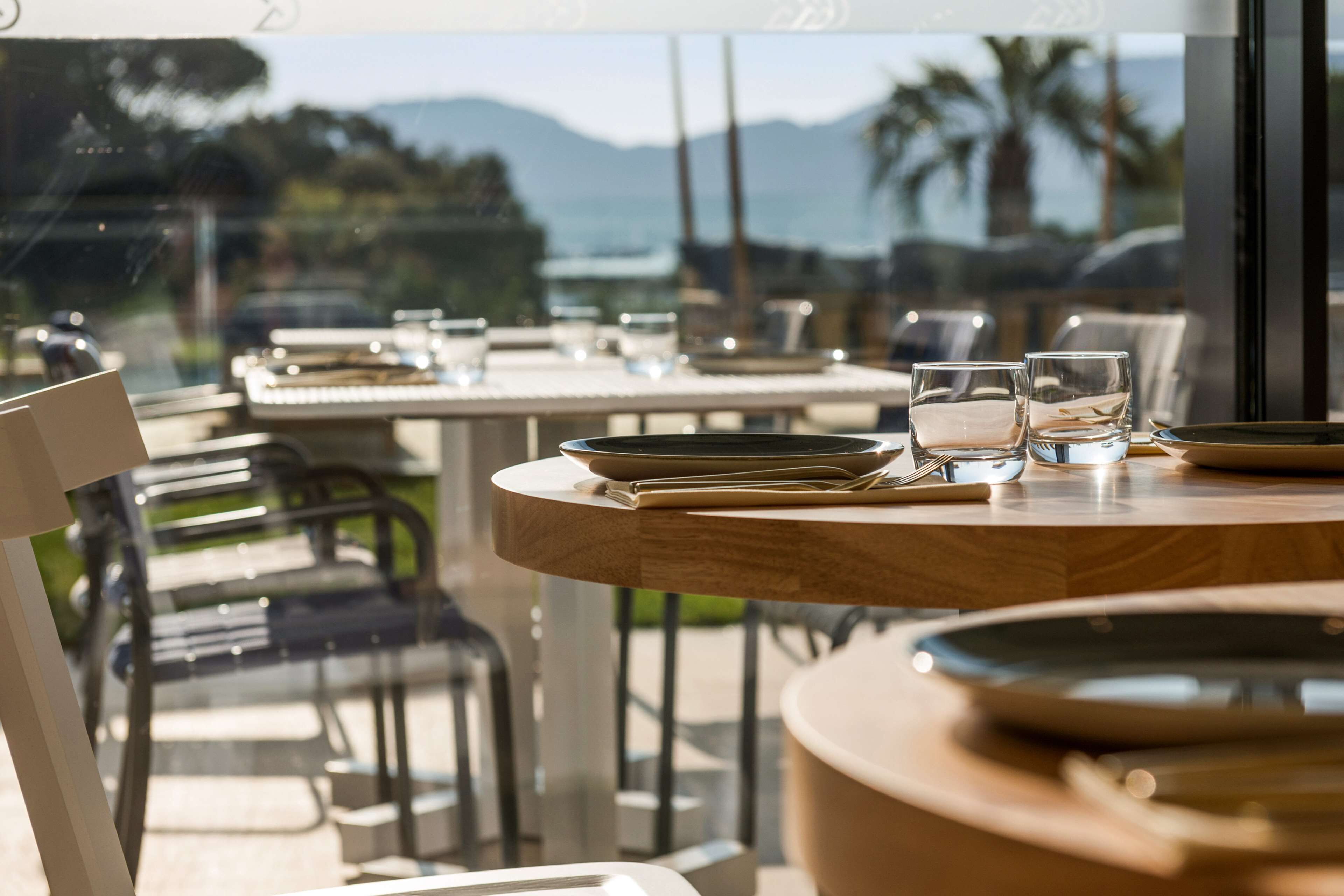 An outdoor dining area with tables and chairs, overlooking a scenic view of mountains and palm trees.