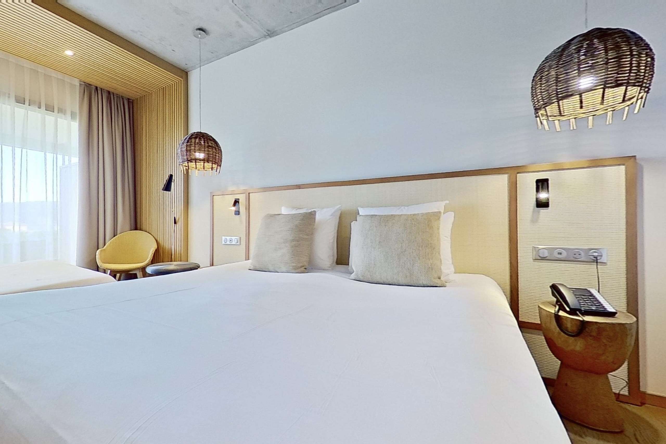 A hotel room with a large bed, two bedside lamps, a bedside phone, and a chair.
