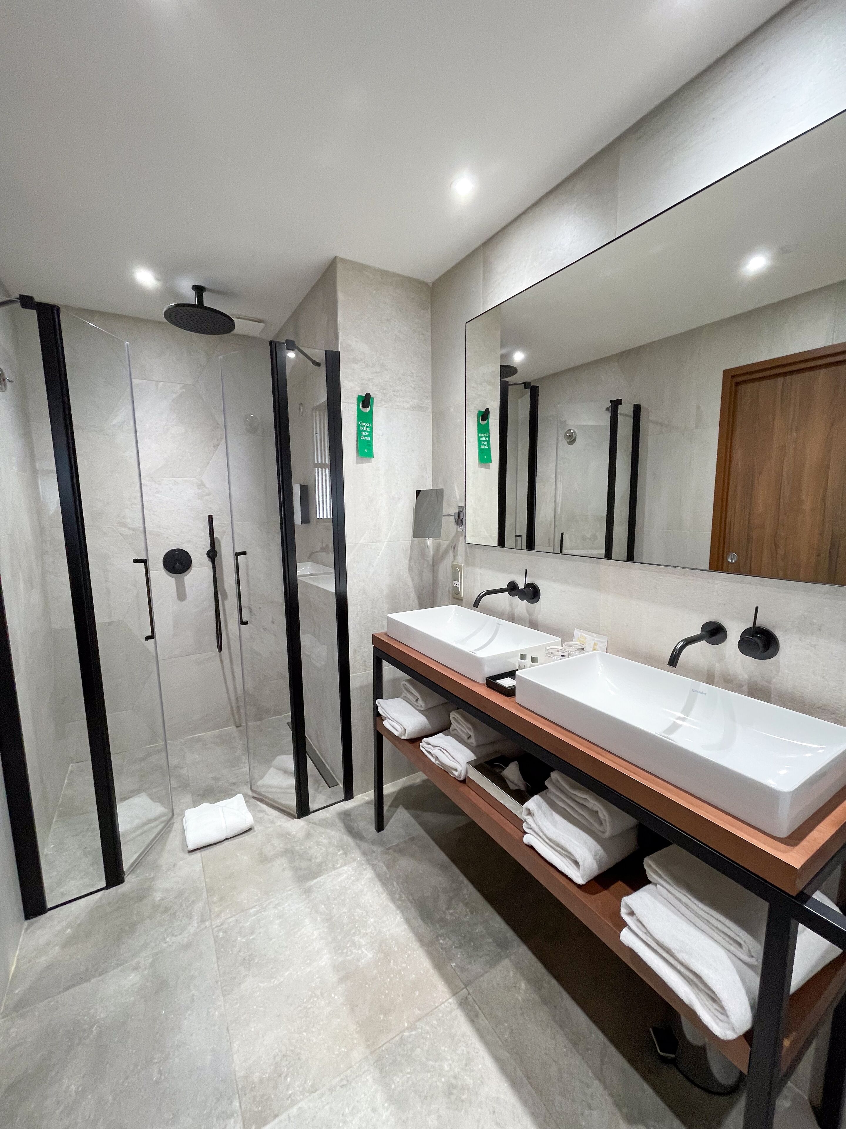Une salle de bain moderne avec une douche à parois de verre, deux lavabos et un grand miroir.