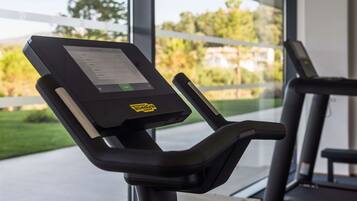 Una bicicleta estática con pantalla digital y vista al exterior a zonas verdes y edificios.