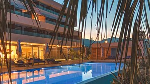 A swimming pool with lounge chairs and umbrellas, surrounded by palm trees and rocks.