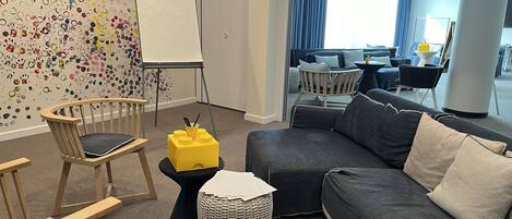 A modern living room with a grey sofa, wooden chairs, a small yellow table, and a colorful wall art piece.