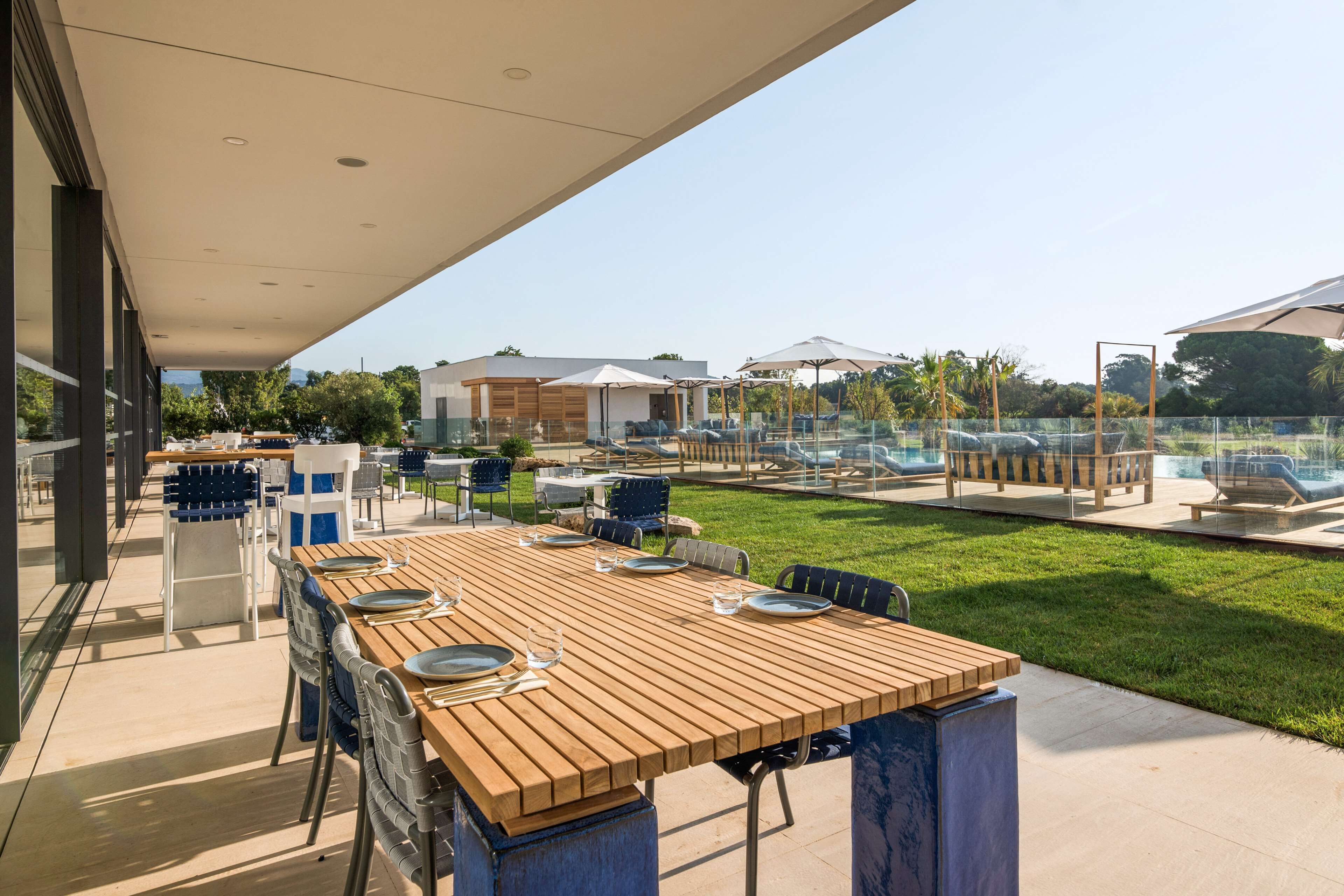 An outdoor dining area with a wooden table and chairs, a pool, and umbrellas.