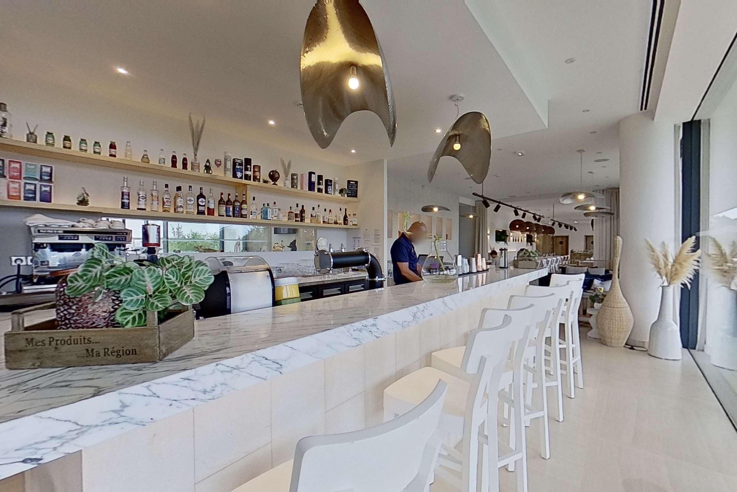 Zona bar moderna con bancone in marmo, sgabelli bianchi e diverse bottiglie sugli scaffali.