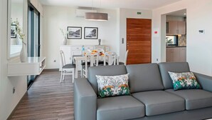 A modern living room with a grey sofa, a dining area with white chairs, and a wooden door.