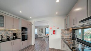 A modern kitchen with light-colored cabinets, a central island with a sink, and a view of the sea through large windows.