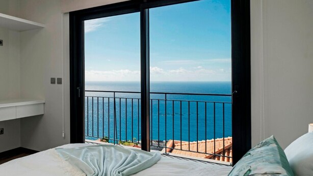 A bedroom with a large sliding glass door leading to a balcony with a view of the ocean.