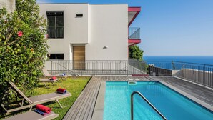 A modern building with a swimming pool, lounge chairs, and a view of the sea.