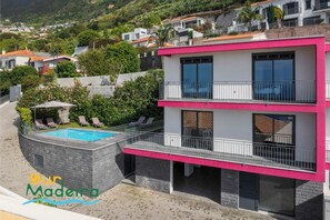 A modern two-story building with a swimming pool, surrounded by greenery and other residential buildings. - Contemporary villa in Calheta | Amaro Sunset (Arco Da Calheta)