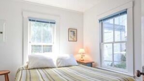 A bedroom with a bed, two windows, a nightstand with a lamp, and a framed picture on the wall. - Beachfront with shared sundeck! (Provincetown)
