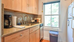 A kitchen with wooden cabinets, a granite countertop, a coffee maker, a sink, and a window with a view of greenery. - Beachfront with shared sundeck! (Provincetown)
