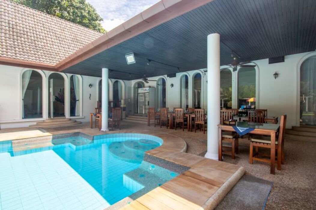 A covered outdoor swimming pool area with a pool, seating, and a covered patio.