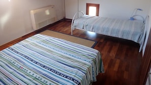 Um quarto pequeno e acolhedor com teto de madeira, uma cama com colcha listrada, um radiador e uma janela.