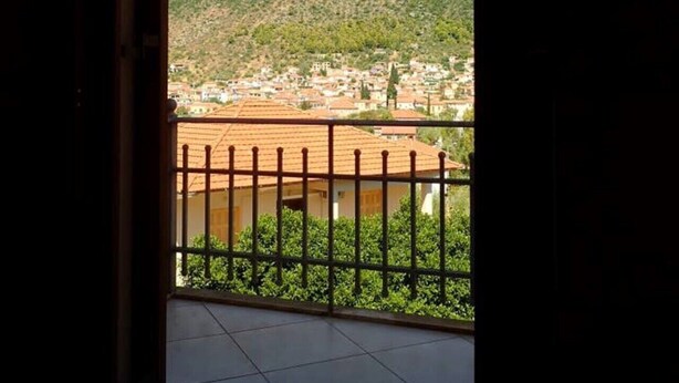 Vista de uma varanda com guarda-corpo de metal, com vista para uma cidade, edifícios e uma montanha ao fundo.