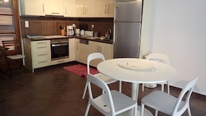 Uma cozinha moderna com armários brancos, uma geladeira de aço inoxidável, forno embutido e uma mesa de jantar redonda com cadeiras brancas.