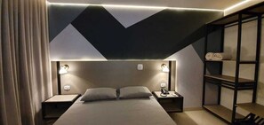 A modern hotel room with a bed, bedside tables, a nightstand, and a built-in shelving unit. - Hotel Cancioneiro (Sinop)