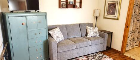A living room with a grey sofa, a blue cabinet, a flat-screen TV, a decorative shelf, a lamp, and a framed picture on the wall.