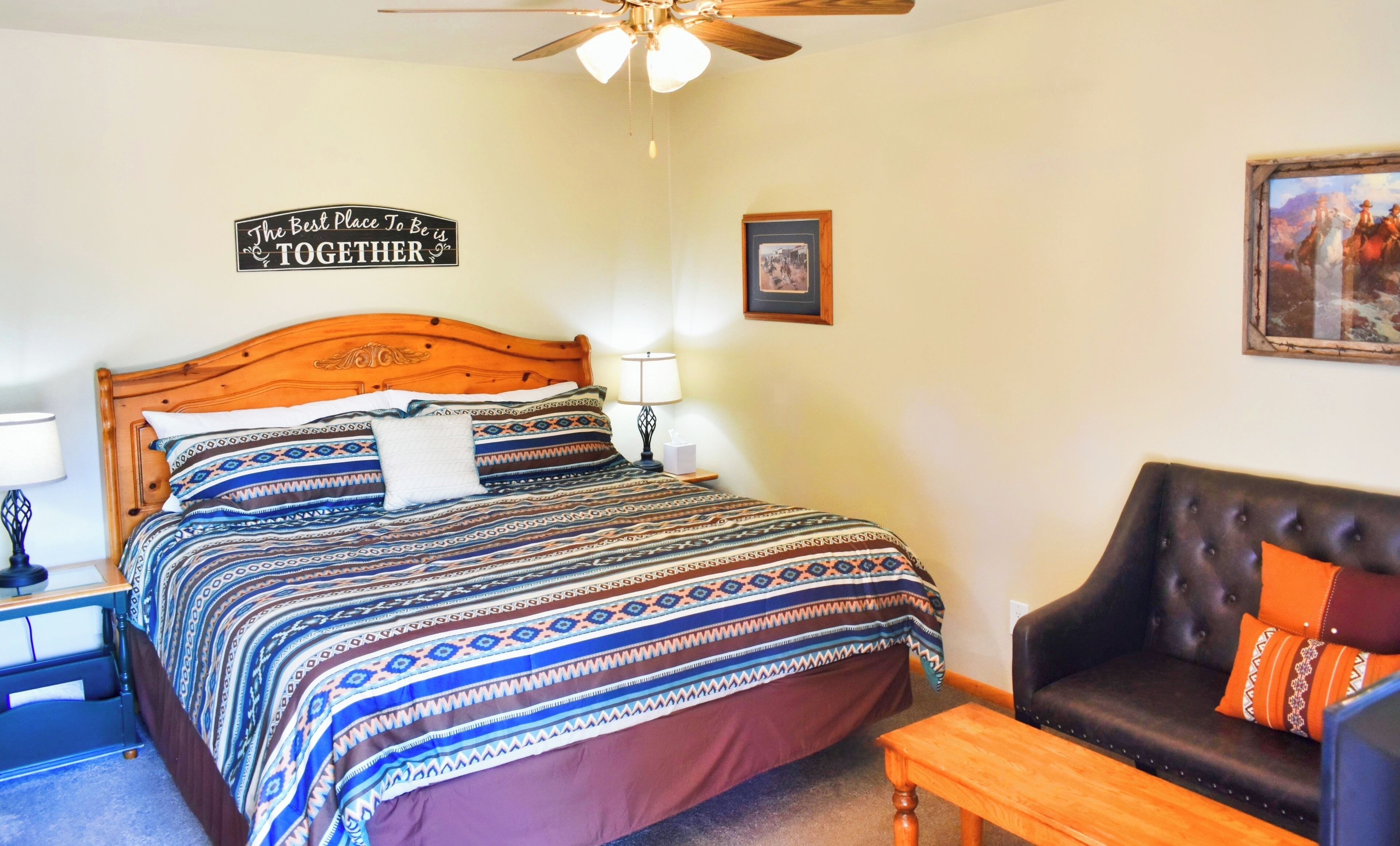 A bedroom with a wooden bed, patterned bedding, a ceiling fan, a framed picture, and a leather sofa.