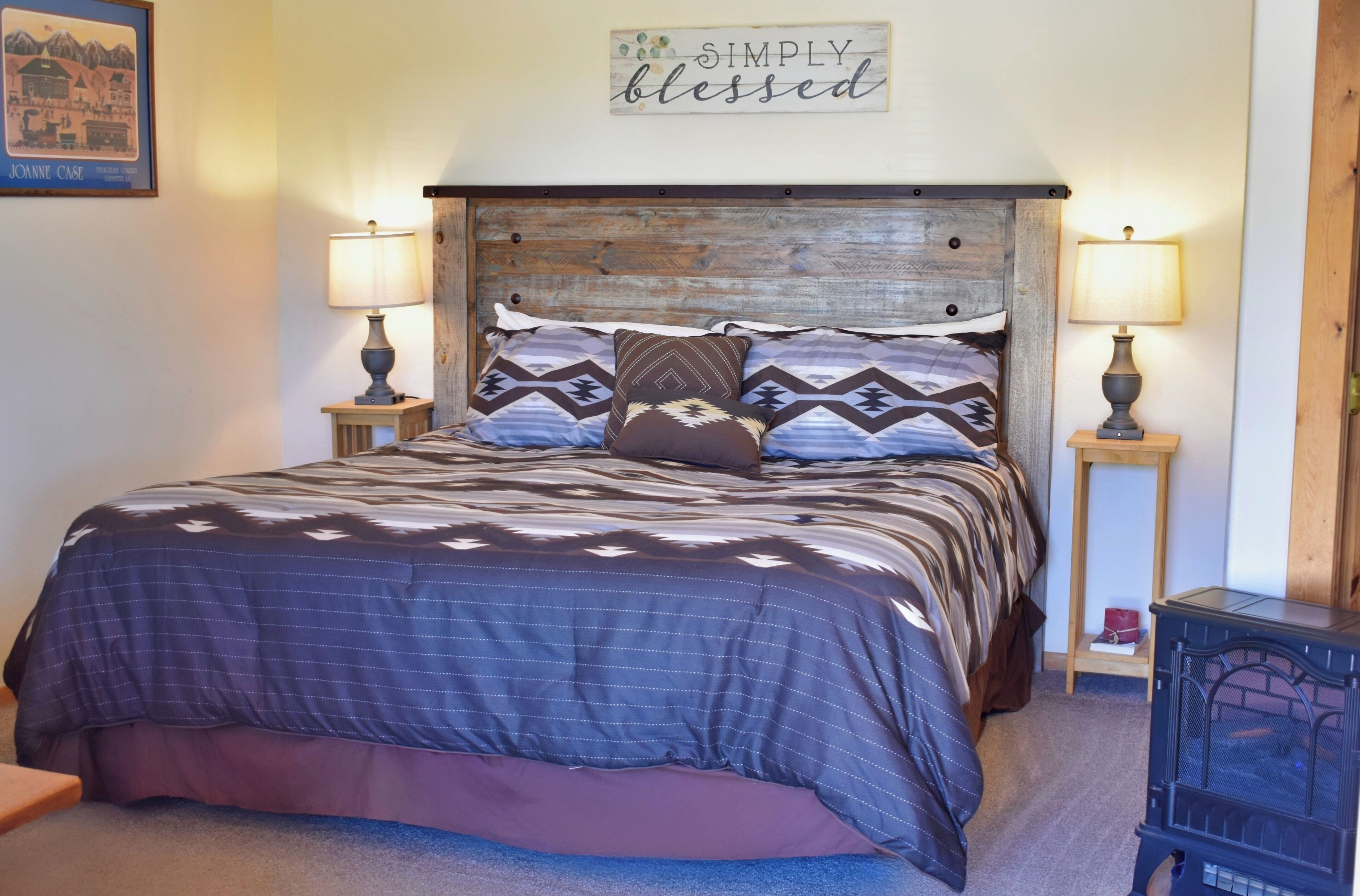 A bedroom with a bed, two bedside tables, a wall sign, and a lamp.