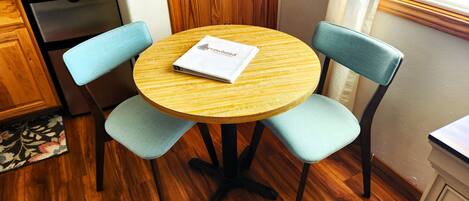 A round wooden table with four light blue upholstered chairs, a booklet on the table, and a wooden cabinet in the background.
