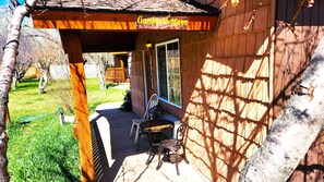 A wooden building with a sign reading "Garden Cottage." There is a covered patio with two chairs and a table.