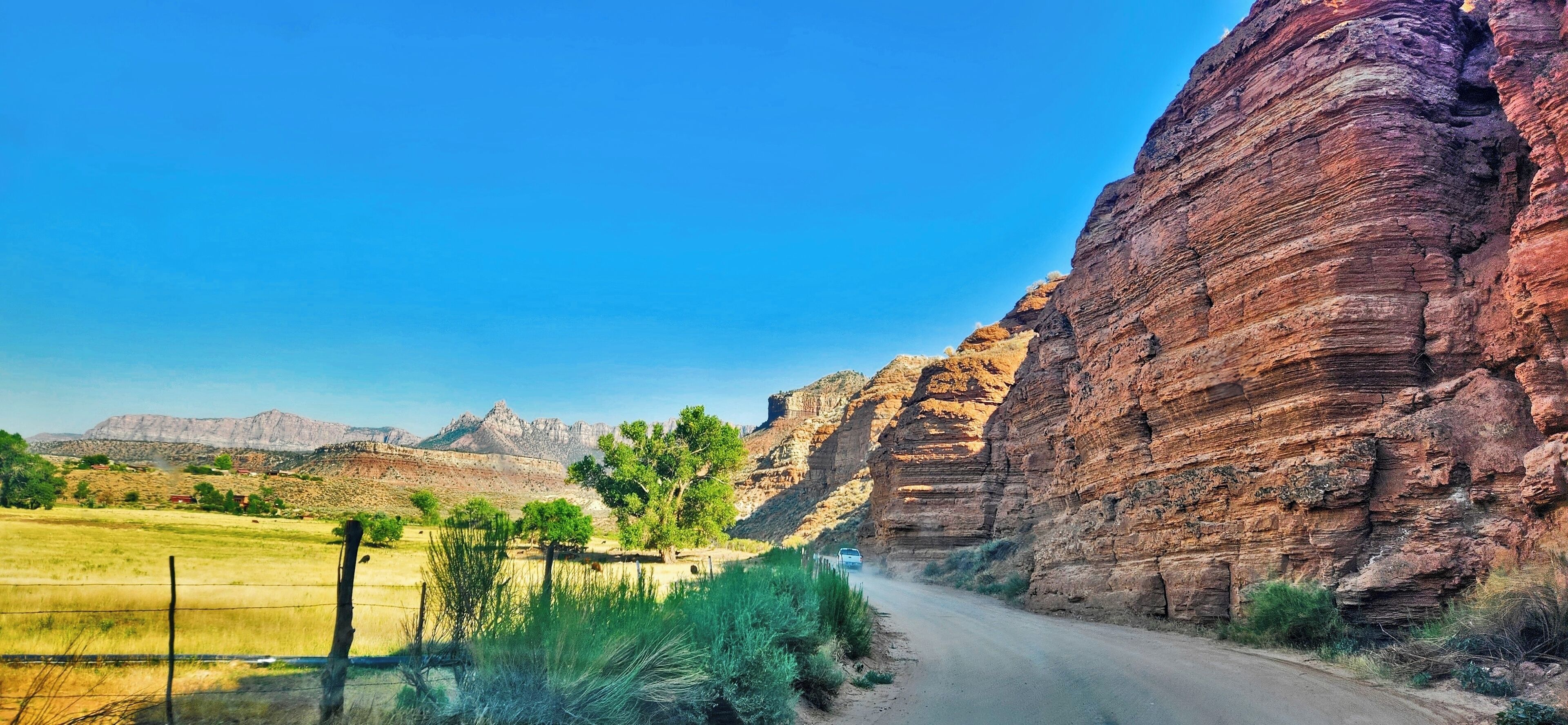 A road flanked by red rock formations and sparse vegetation.