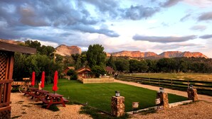 A rustic lodge with picnic tables and red umbrellas, surrounded by a fenced lawn and mountains in the background. - Arrowhead Country Cabins (Mount Carmel)
