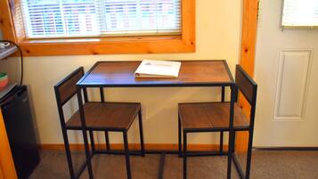 Une petite pièce avec une table en bois et deux chaises, une fenêtre avec des stores et une porte.