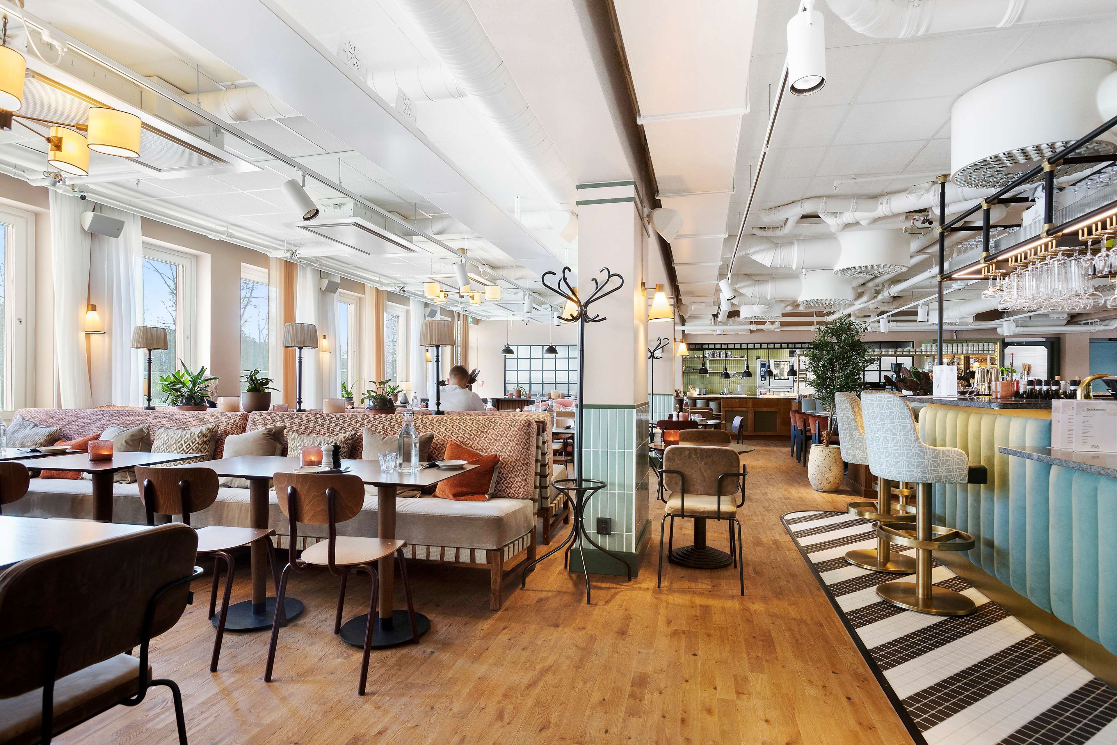 Un restaurant spacieux avec de hauts plafonds, des conduits apparents et différents types de sièges, notamment des tables, des banquettes et des places au bar.