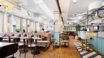 Un restaurante espacioso con techos altos, conductos a la vista y una variedad de opciones de asientos, incluyendo mesas, cabinas y asientos en la barra.