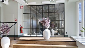 A modern interior with wooden steps leading to a glass door, white vases with flowers, and a fire extinguisher on the wall. - Hotel Gio, BW Signature Collection (Solna)