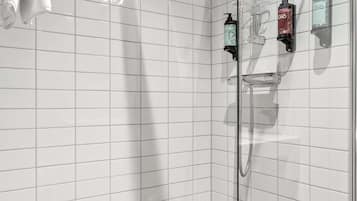 Un área de ducha moderna con mampara de vidrio, paredes cubiertas de azulejos blancos y piso de baldosas marrones.