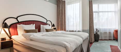 Habitación de hotel moderna con una cama grande, una mesita de noche, una lámpara y vistas al exterior a través de amplios ventanales.