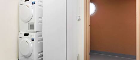 Un lavadero con lavadoras y secadoras apiladas, una puerta que da a otra habitación y un suelo de baldosas verdes.