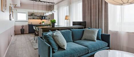 Un salon moderne avec un canapé de couleur turquoise, une table basse en marbre et une cuisine en arrière-plan.
