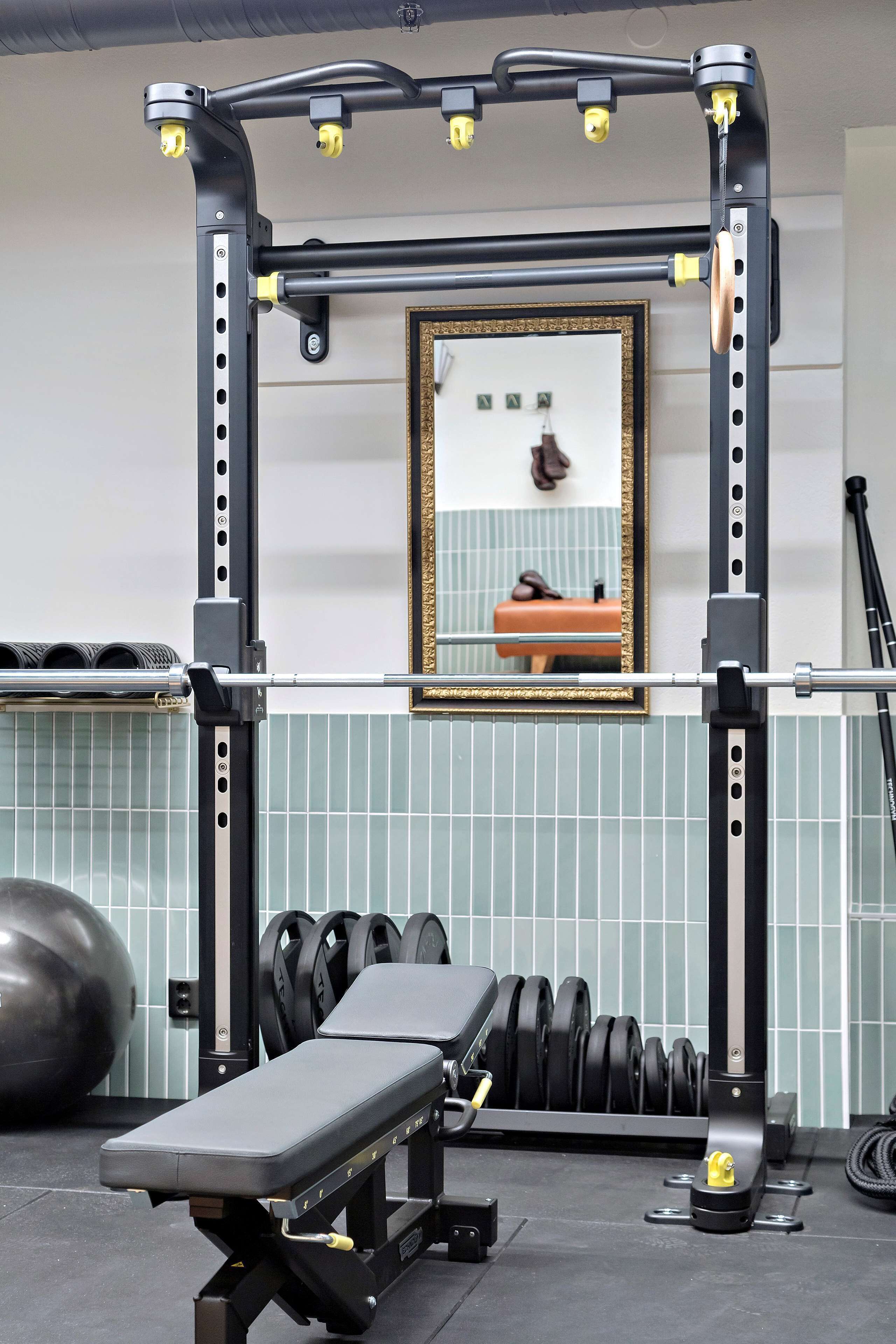 A gym with a bench press, weight racks, and a mirror on the wall.