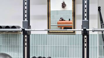 Un gimnasio con una prensa de banca, estantes para pesas y un espejo en la pared.