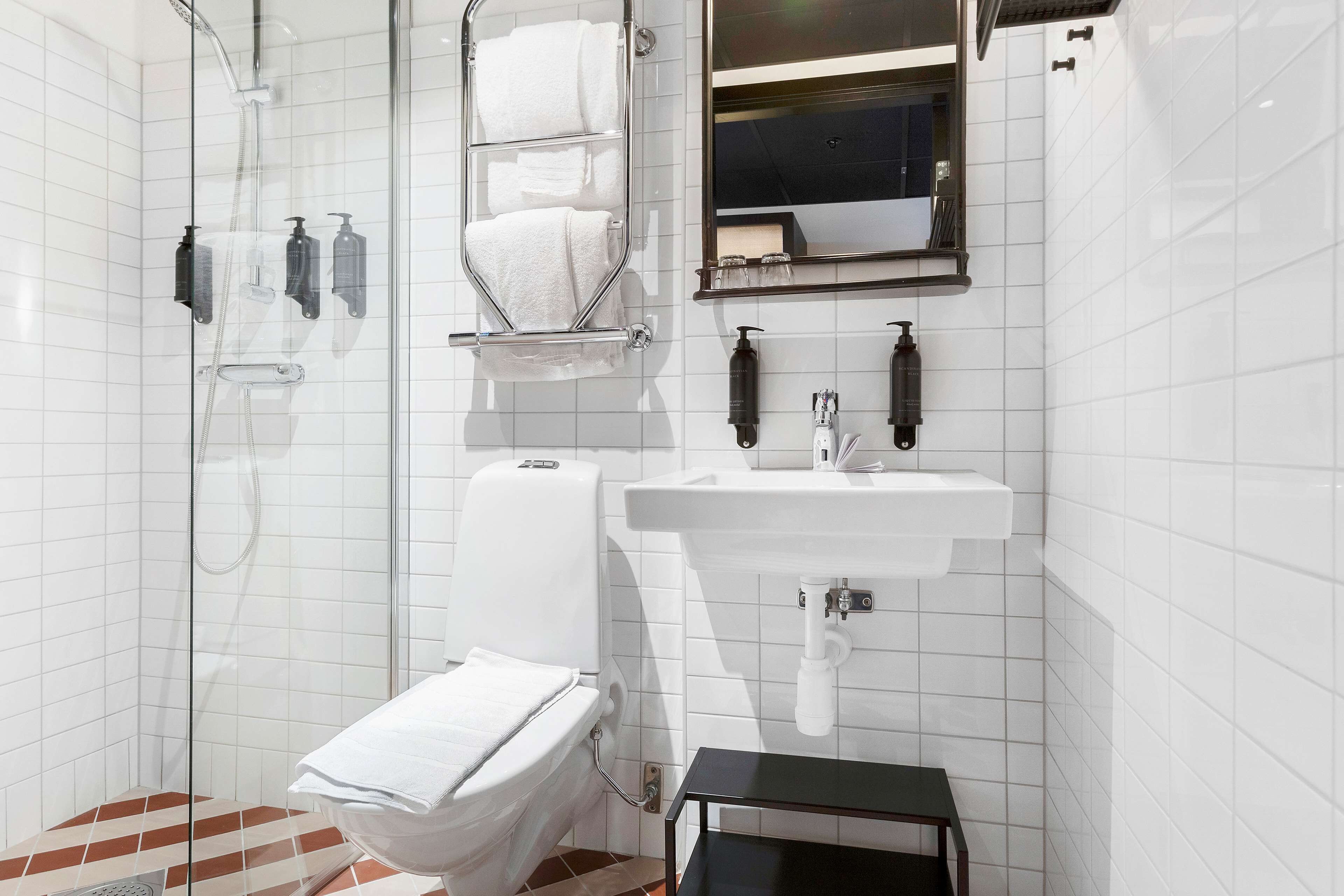 Ein modernes Badezimmer mit einer Duschkabine aus Glas, weißen Fliesen, einer Toilette, einem Waschbecken und einem kleinen schwarzen Tisch.