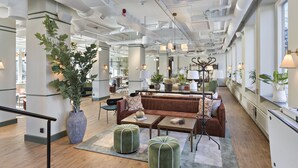 A spacious lobby with a brown sofa, green ottomans, and a large potted plant. - Hotel Gio, BW Signature Collection (Solna)