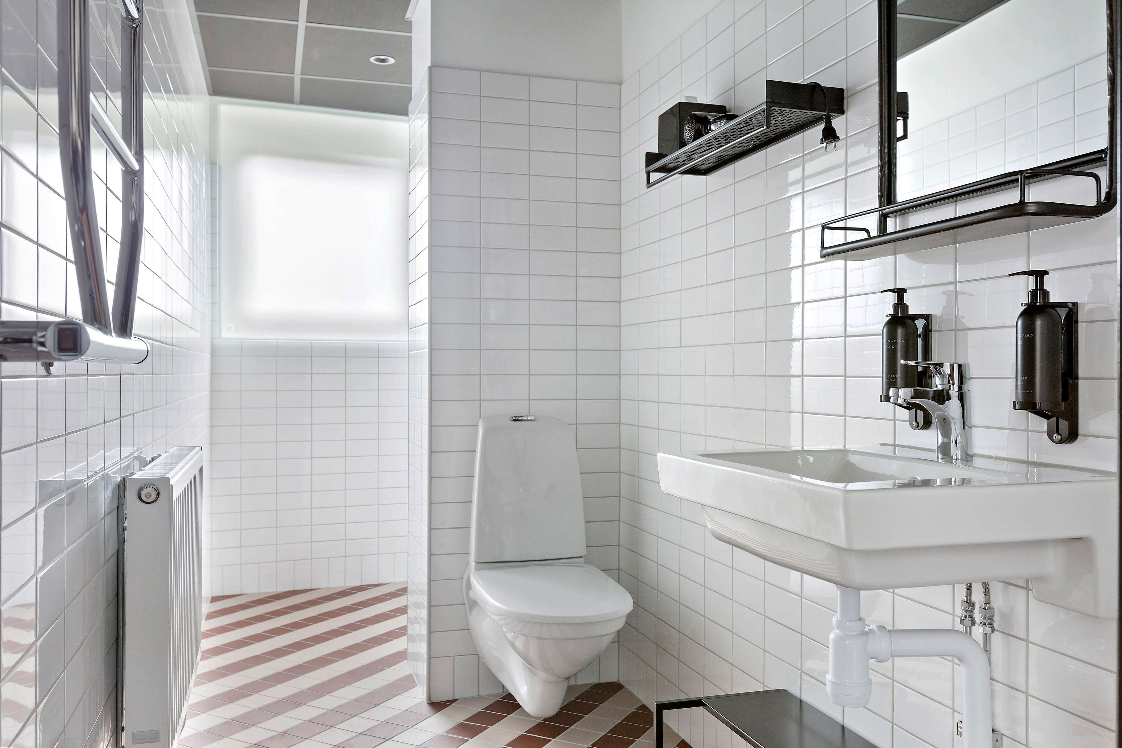 A modern bathroom with white tiles, a white toilet, a sink with a mirror, and a radiator.