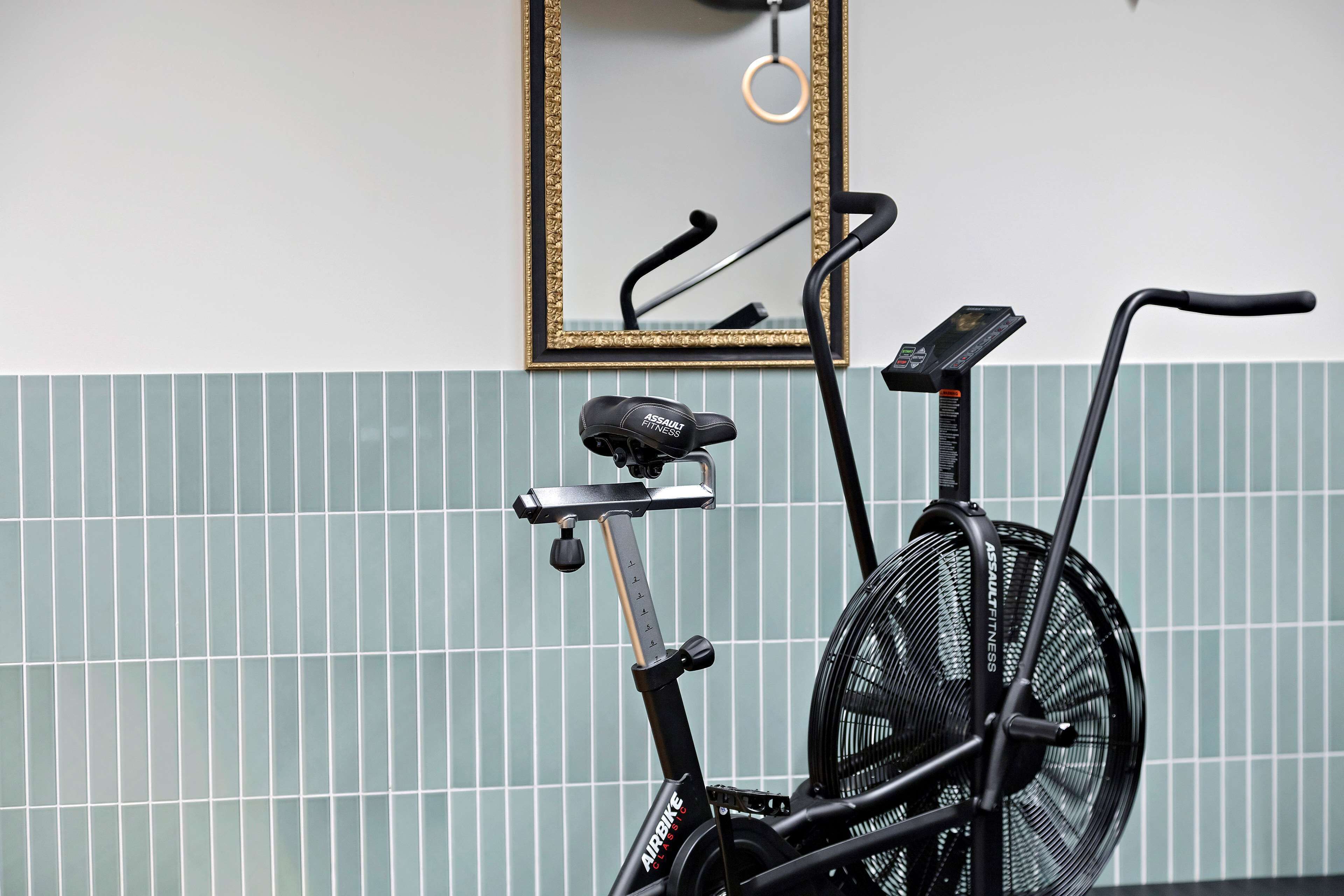 Uma bicicleta ergométrica com visor digital, um espelho e um revestimento de azulejos.