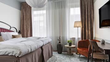 Una habitación de hotel con una cama grande, un escritorio, una silla, una lámpara y un jarrón con una planta.