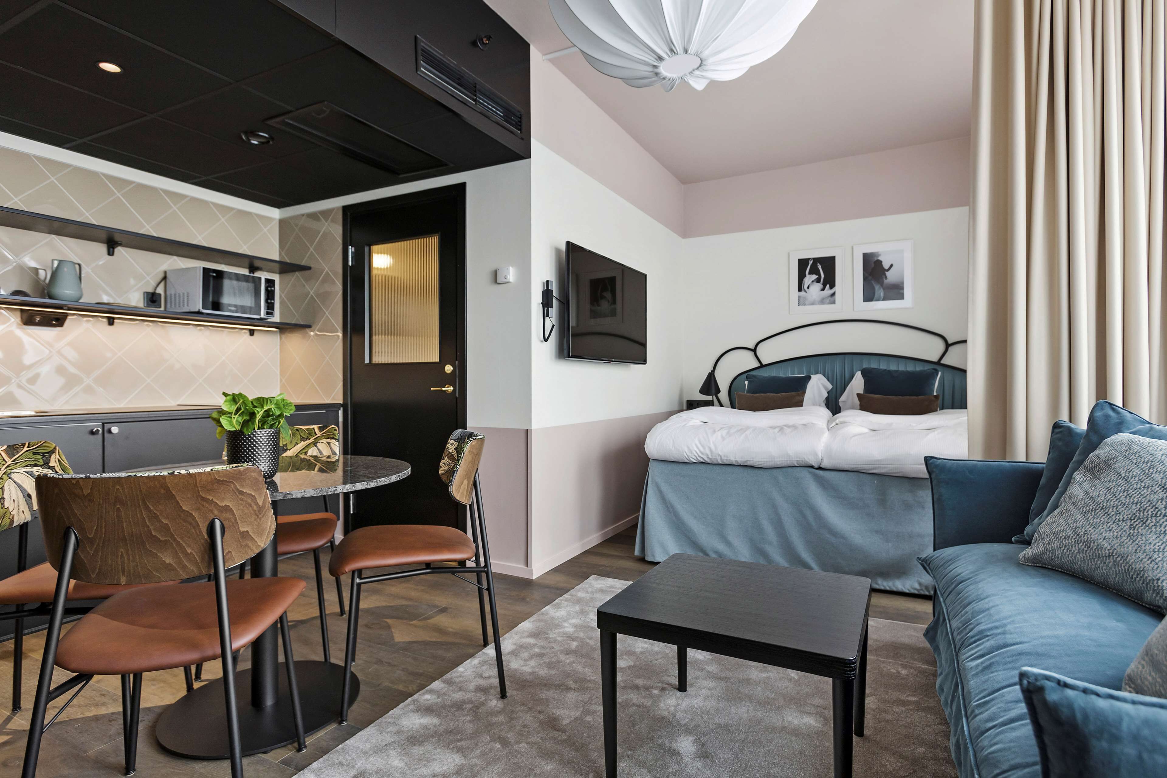 Una camera d'albergo moderna con angolo cottura, zona pranzo con sedie, divano, letto e televisione appesa al muro.