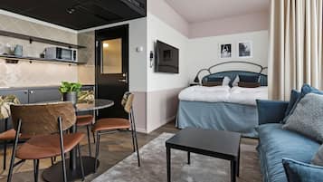 Una camera d'albergo moderna con angolo cottura, zona pranzo con sedie, divano, letto e televisione appesa al muro.