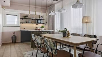 Una cocina moderna con una isla central, luces colgantes y un comedor con mesa de madera y sillas tapizadas.