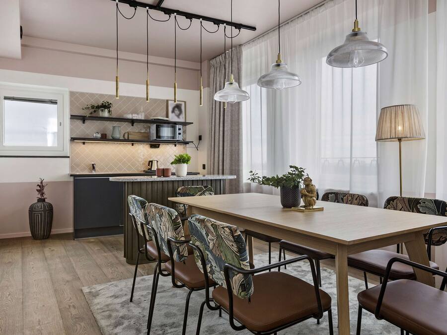 Una cocina moderna con una isla central, luces colgantes y un comedor con mesa de madera y sillas tapizadas.