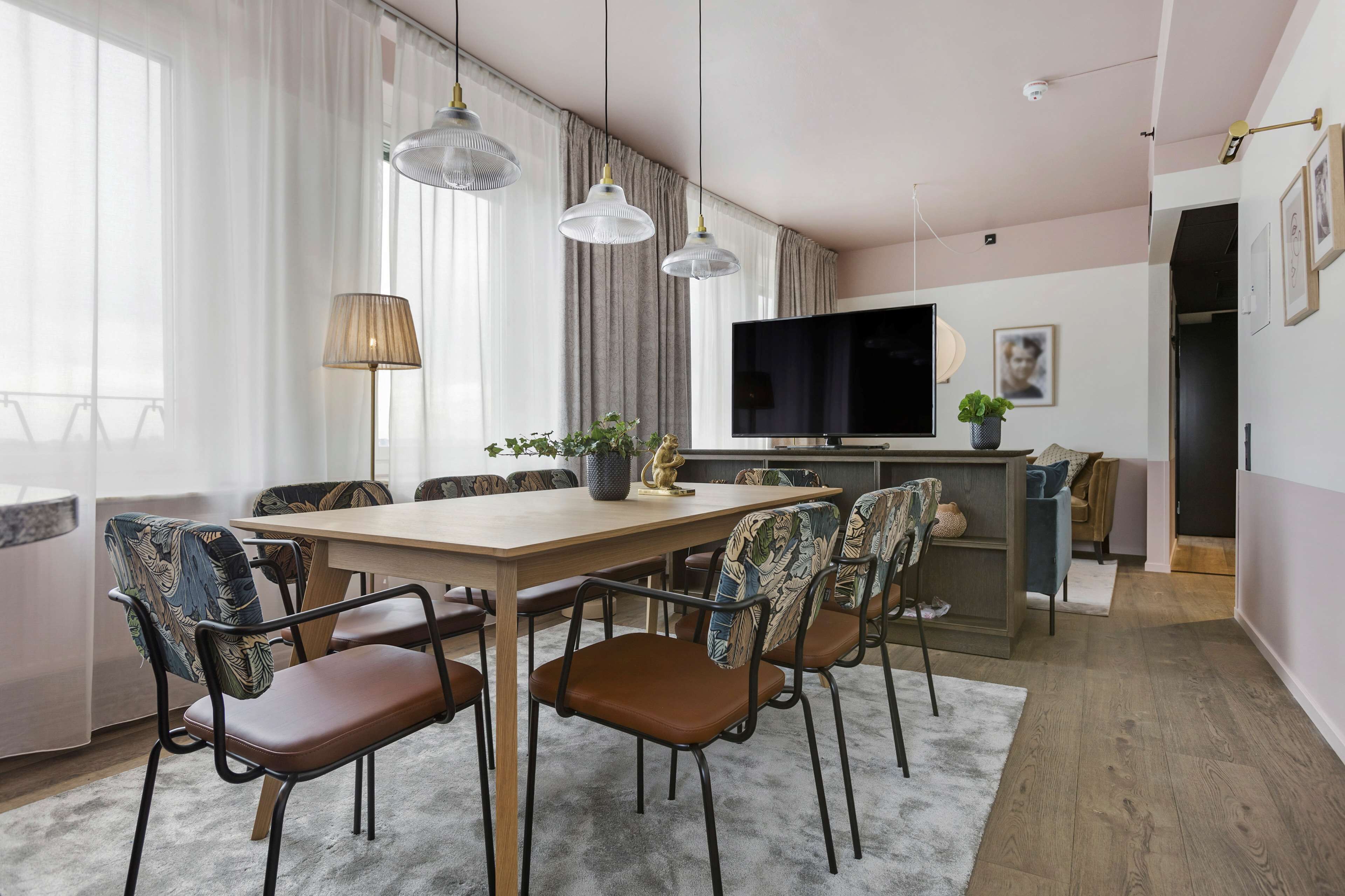 A modern dining area with a wooden table, brown chairs, and a large flat-screen TV.
